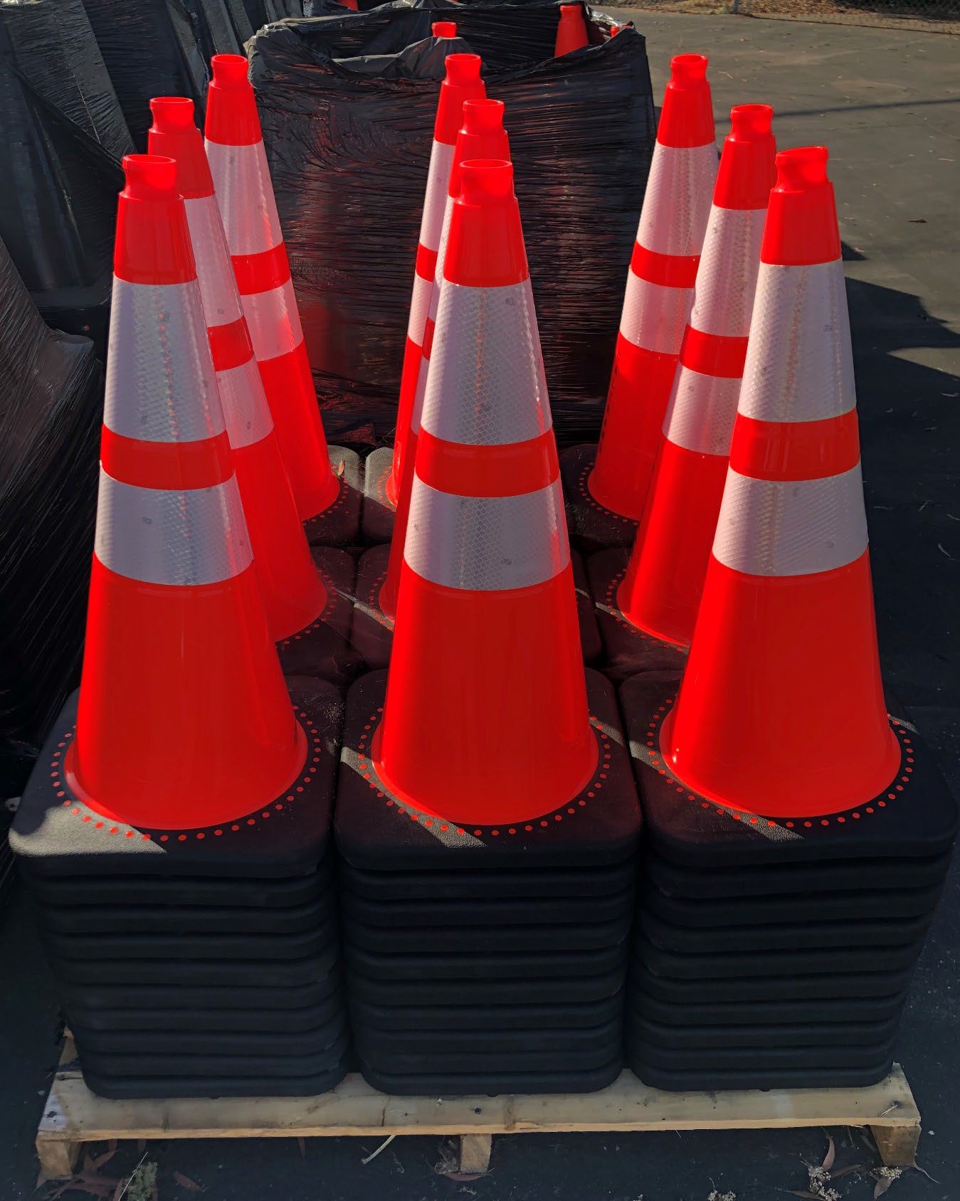 Photograph of new 28-inch traffic cones with reflective collars stacked upright in groups on pallets of black cone bases.